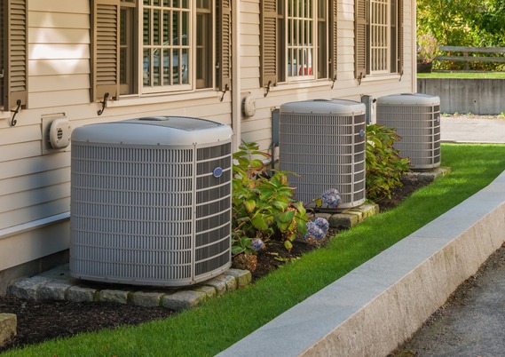 The side of a house features three air conditioning units and surrounding plants.