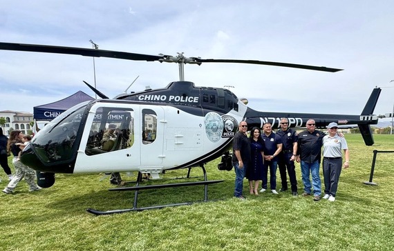 Group stands beside a Chino Police helicopter during a community event held on a grassy field.