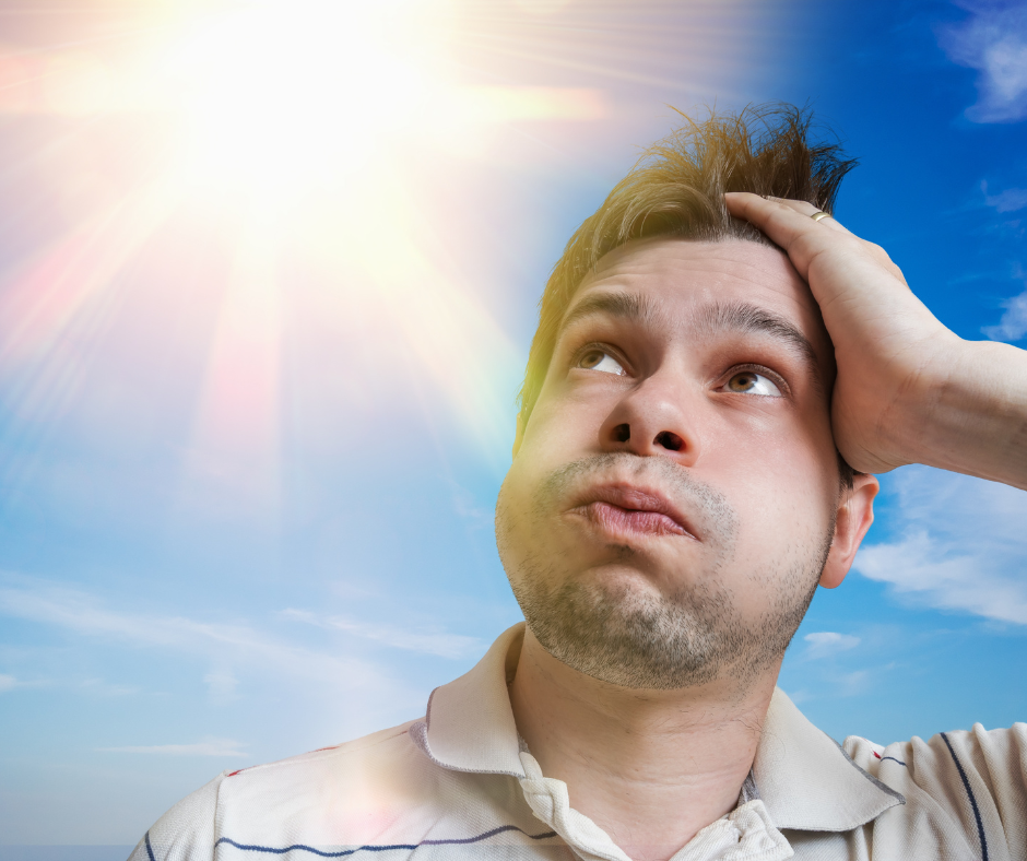 A man in a striped shirt runs his fingers through his hair while he sits below a blazing hot summer sun