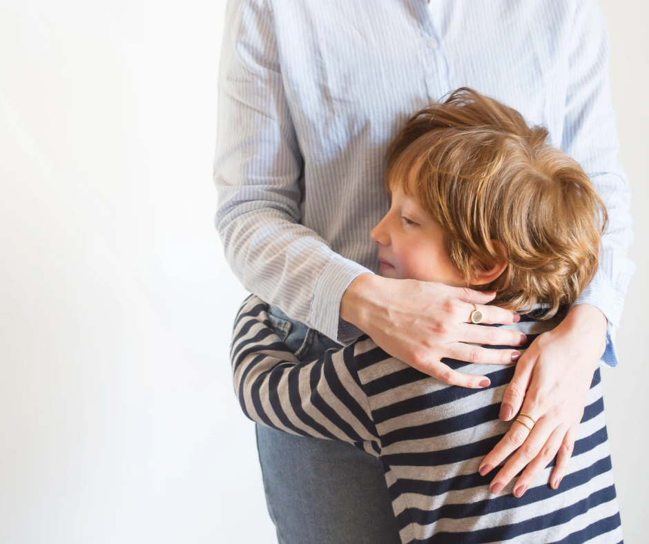 The torso of a grown woman hugs a redhead child wearing a striped shirt.