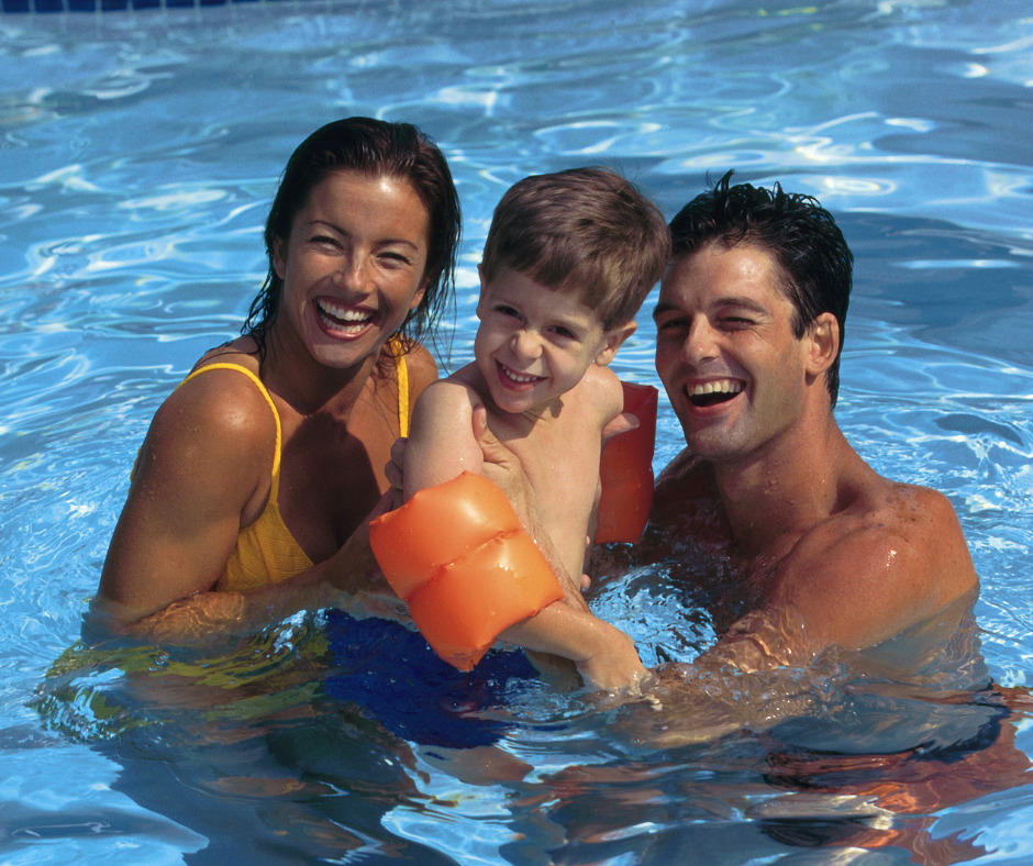 A very attractive woman and man hold a child in a swimming pool. The kid is wearing yellow water wings.