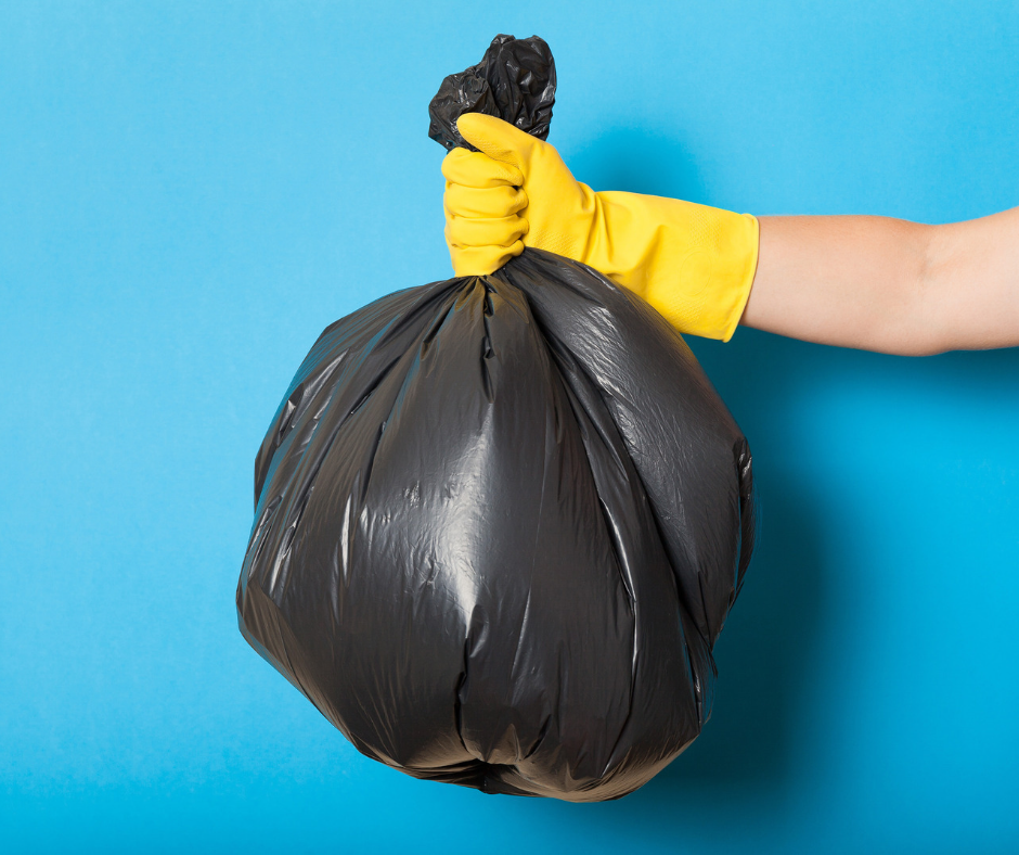 A single black trash bag is held aloft by a yellow-gloved hand against a light blue background