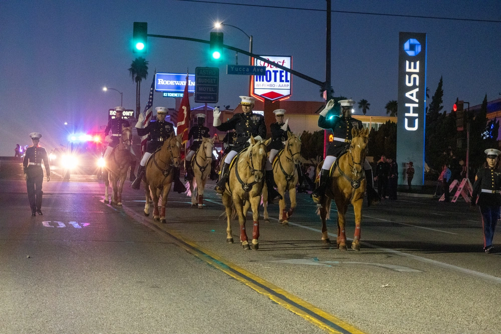 Military personnel ride horses in a nighttime street parade, with police vehicles flashing lights and Rodeway Inn and Chase signs in the background.