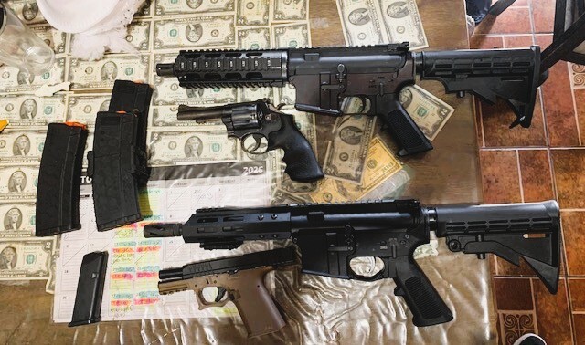 Firearms and accessories are displayed on a table covered with cash.