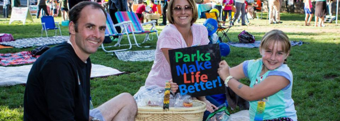 Family Sitting on Lawn Holding Parks Make Life Better Sign