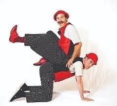 Two men in black pants and red vests performing a circus trick