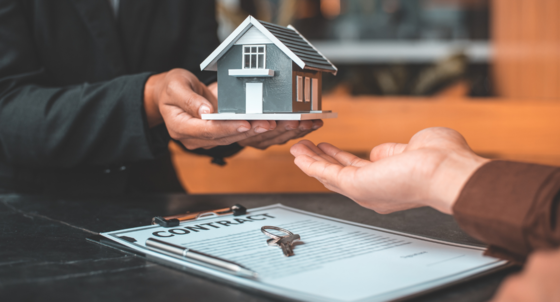 Stock photo of representing a landlord and tenant handing over a toy house with a contract underneath