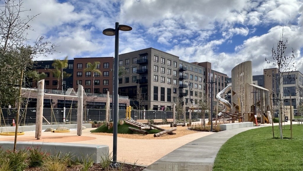 Modern playground with wooden play structures, rope swings, and a tall spiral slide