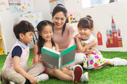a woman and three children reading a book on a green floor