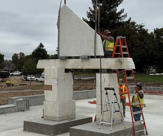Large white geometric stone sculptural shapes being installed in park setting.