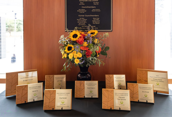 Sunnyvale Community Awards plaques displayed on a table with a colorful flower arrangement beneath a City Council recognition wall.