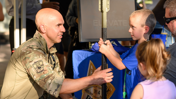 Law enforcement agent bends to show a piece of equipment to a young resident