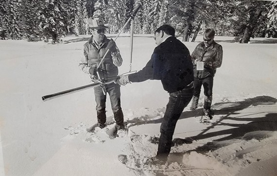 A black and white photo of people taking a snow survey.