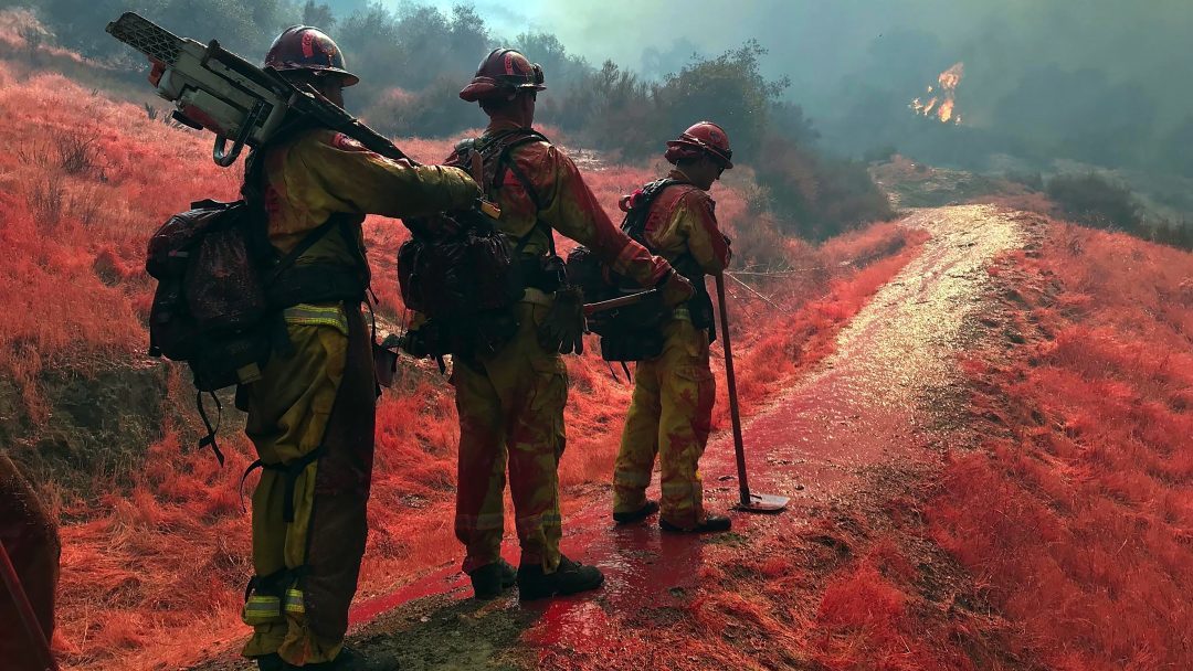 Three California Conservation Corpsmember stand on a trail covered in fire retardant 