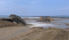 Photograph of bulldozer moving sand on a beach.