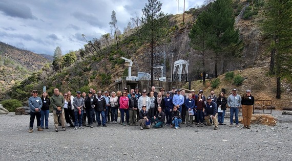 Group photo of tour participants on gravel with Indian Bar Recreation area on the American River in background.