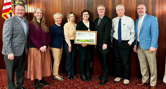 People posing with a woman holding a retirement gift