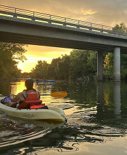 Kayaker on a river approaching a bridge at sunset