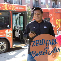 Hombre parado mirando su telefono enfrente del autobus JUMP, logo de tarifa gratuita para mejorar la calidad del aire
