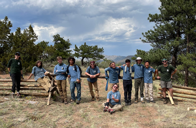 Youth Corps team standing in front of a fence in the foothills