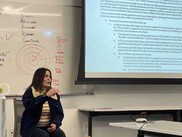 Kim Sanchez sitting next to white board presenting information
