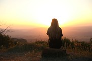 woman sitting on mountain looking at sunset