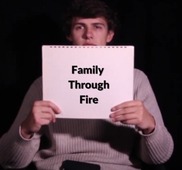 Film student holding up sign that says "Family Through Fire" the name of their documentary