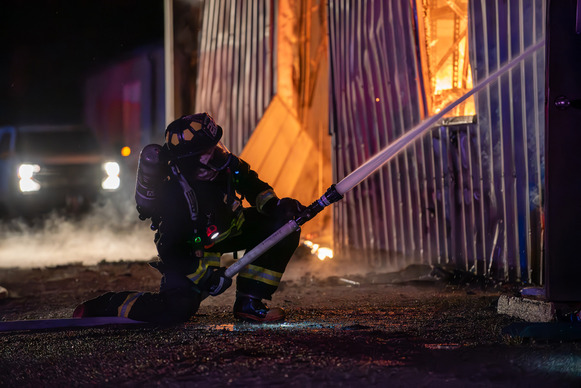 Firefighter in bunker gear putting out a shed fire with a high pressure hose