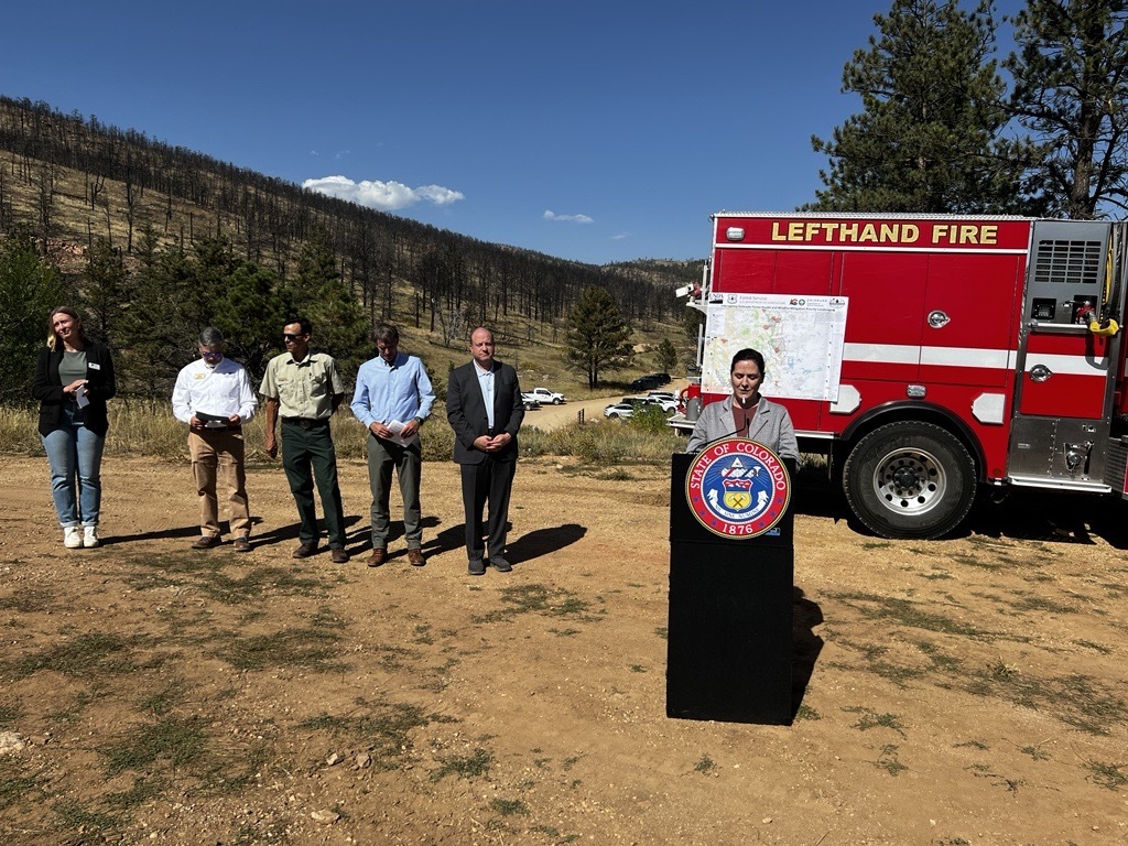 Commissioner Stolzmann at podium speaking to audience at Heil Valley Ranch. Firetruck in background.