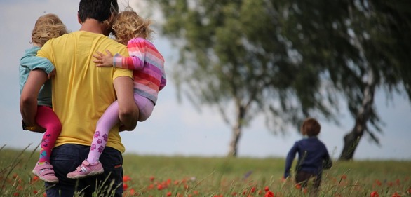 man holding two kids on a flower filed