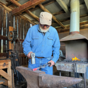 Blacksmith volunteer Amos hammers a red hot piece of metal.