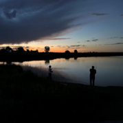 A young boy and a man fish the shore of lake Stearns at sunset. 