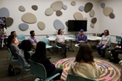 Picture of people sitting around a circular rug and items on the ground