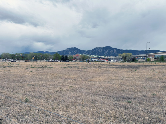 A barren field with yellow straw grasses sits beneath a major Boulder, Colorado road. 