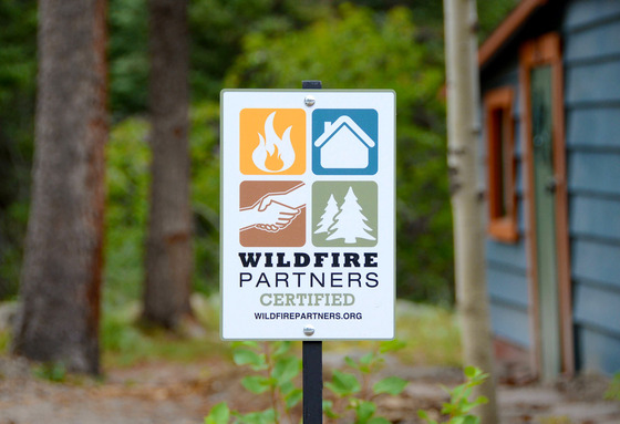 A Wildfire Partners certified yard sign in a wooded forest home setting.