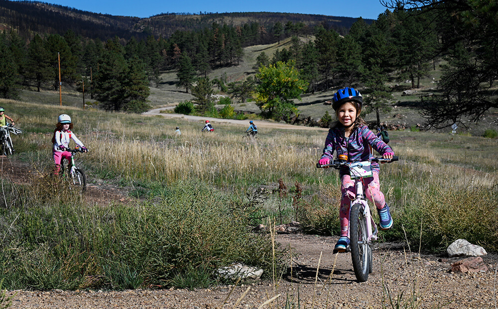 Young kids smile as they ride the trail at Heil Valley Ranch