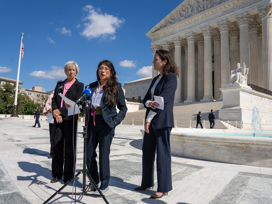Commissioners Marta Loachamin, Claire Levy and Ashley stolzmann stand before a microphone stand in front of the US Supreme Court on Oct. 5, 2026