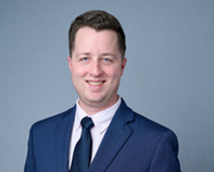 Headshot of Vincent who is standing in front of a light blue background and wearing a suit.