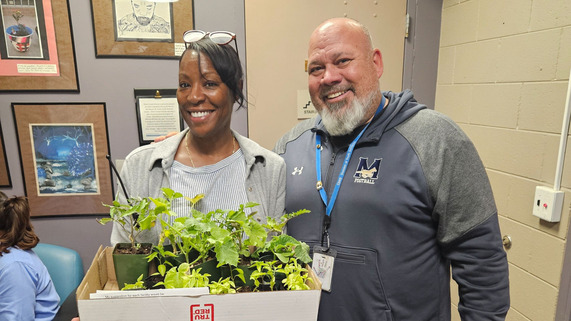 Image of Clare McKendry, School Social Worker and a male staff with a box full of seedlings. 