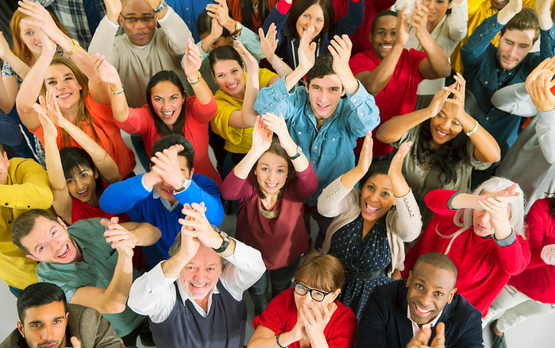 Aerial view of a group of people with diverse genders, ethnicities and ages smiling and clapping their hands above their heads