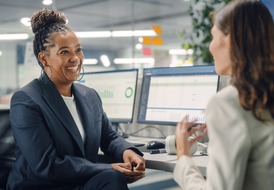 A woman smiles warmly while talking to a colleague in an office setting