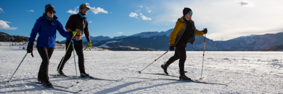 Three people in ski attire stand on a snowy slope, preparing for their descent in a picturesque winter setting.