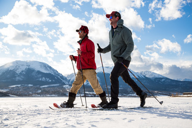 Two men traverse a snowy trail while cross country skiing, highlighting the beauty of winter sports and outdoor activity