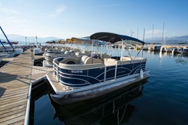 A pontoon boat is securely docked at a wooden dock, surrounded by calm water and a clear sky.