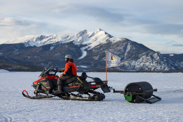 A man riding a snowmobile with a majestic mountain range in the background, showcasing a winter adventure.