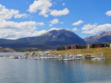 A scenic marina featuring boats docked in front of majestic mountains under a clear blue sky.
