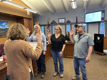 In a courtroom, three people stand with their hands raised, indicating a plea or response during a legal proceeding.