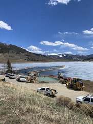 A large construction site with several trucks parked beside a body of water, showcasing ongoing development activities.