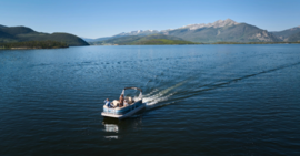 A boat glides across a serene lake, framed by majestic mountains in the background.