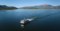 A boat glides across a serene lake, framed by majestic mountains in the background.